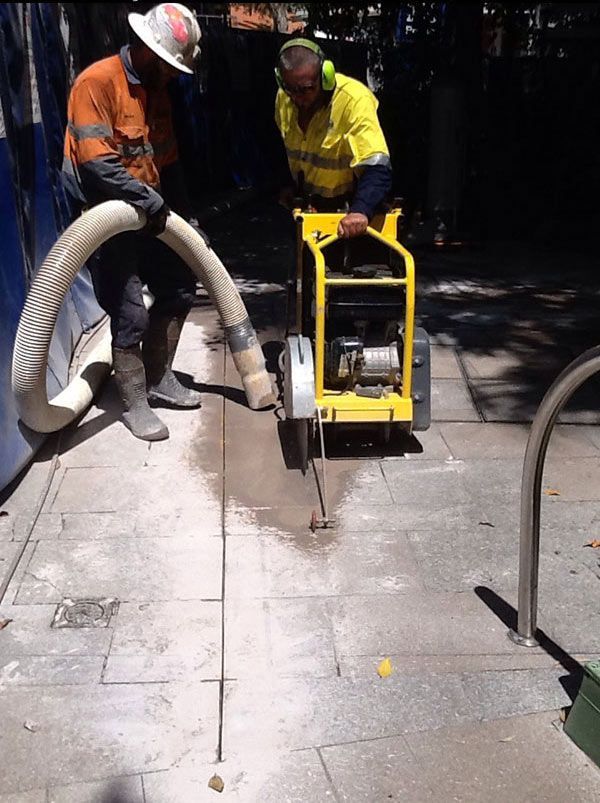 Two men are using a yellow machine to cut concrete