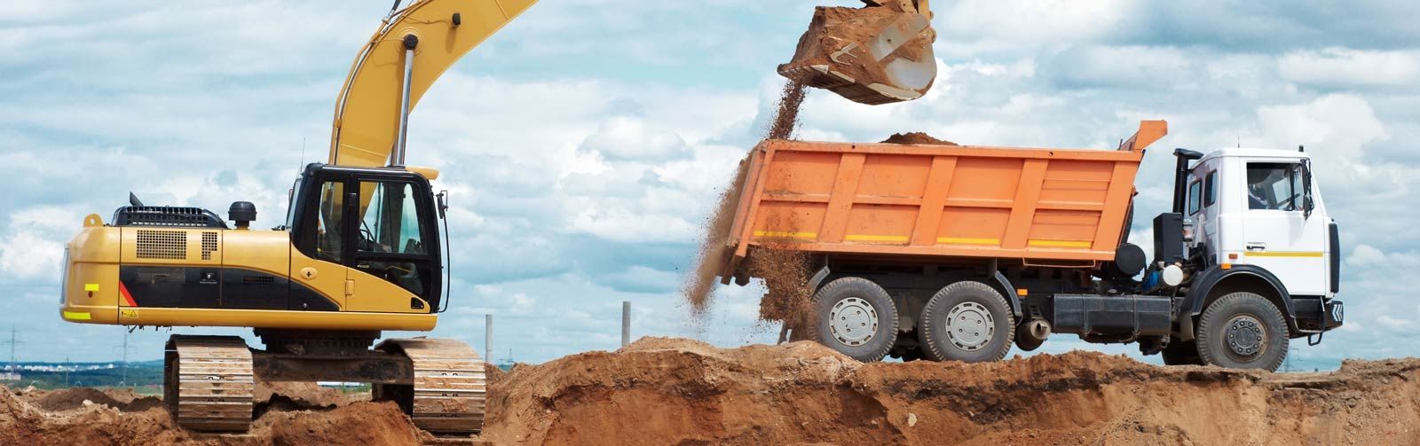 An excavator is loading dirt into a dump truck at a construction site.