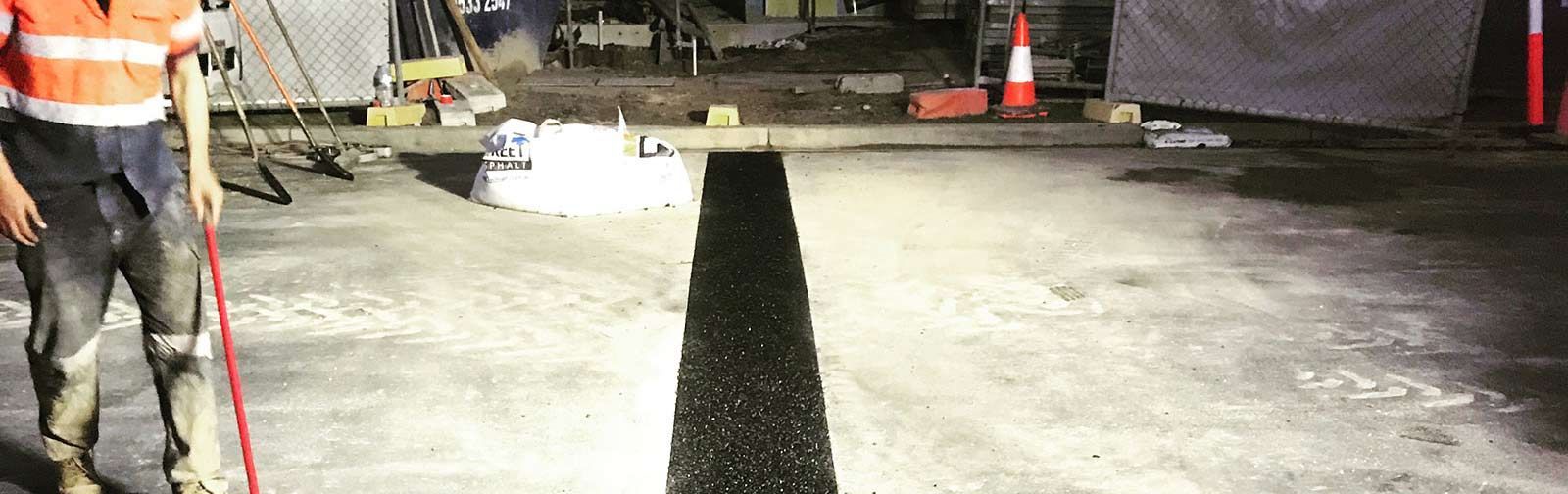 A man is painting a line on the road with a broom.