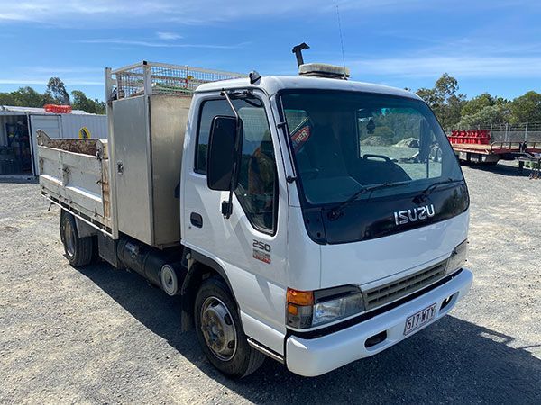 A white isuzu truck is parked in a dirt lot.