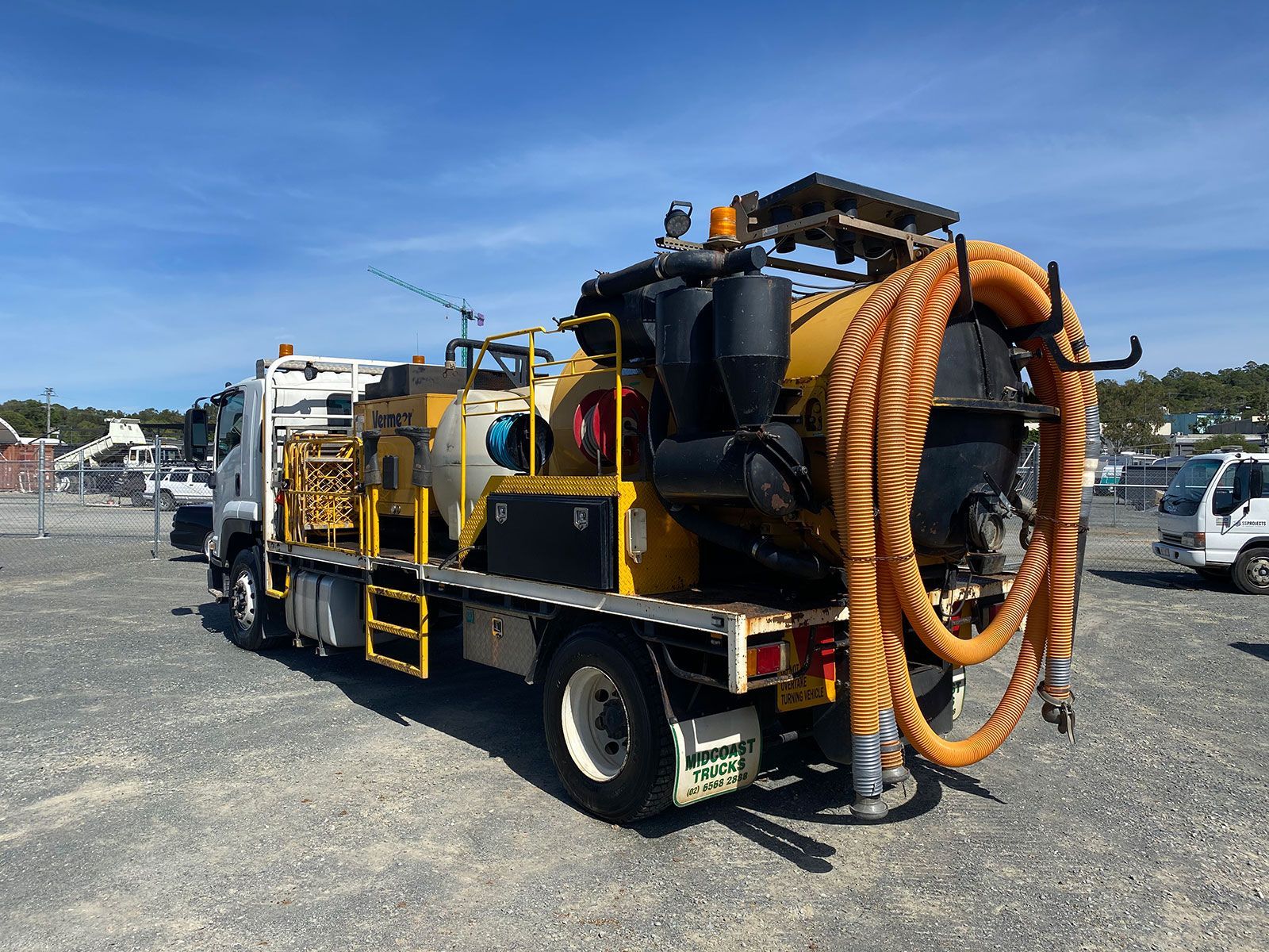 A yellow and black truck with a hose attached to it is parked in a gravel lot.