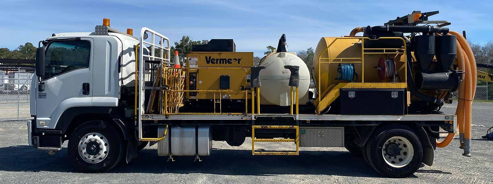 A vacuum truck is parked in a gravel lot.