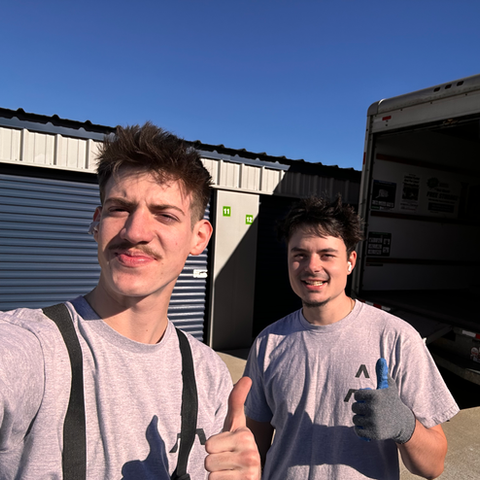 Two men are giving a thumbs up in front of a moving truck