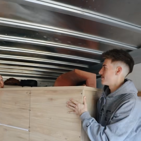A man in a grey sweatshirt is holding a wooden box