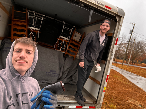 Two men are standing in the back of a moving truck.