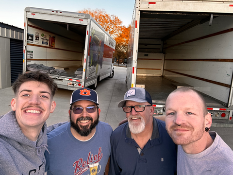 A group of men are posing for a picture in front of a moving truck.