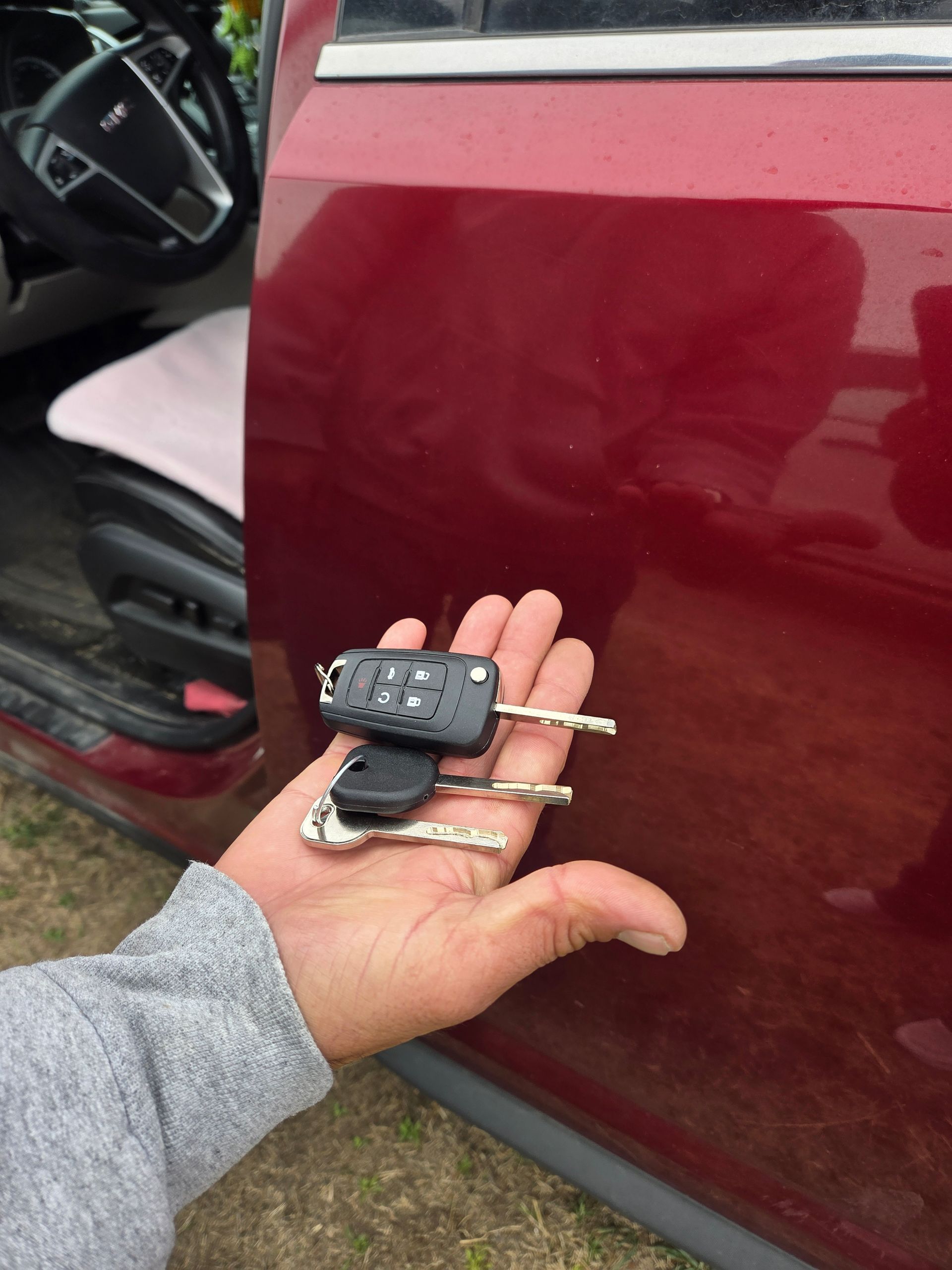 Hand holding a black car key fob beside a red car door with the door open