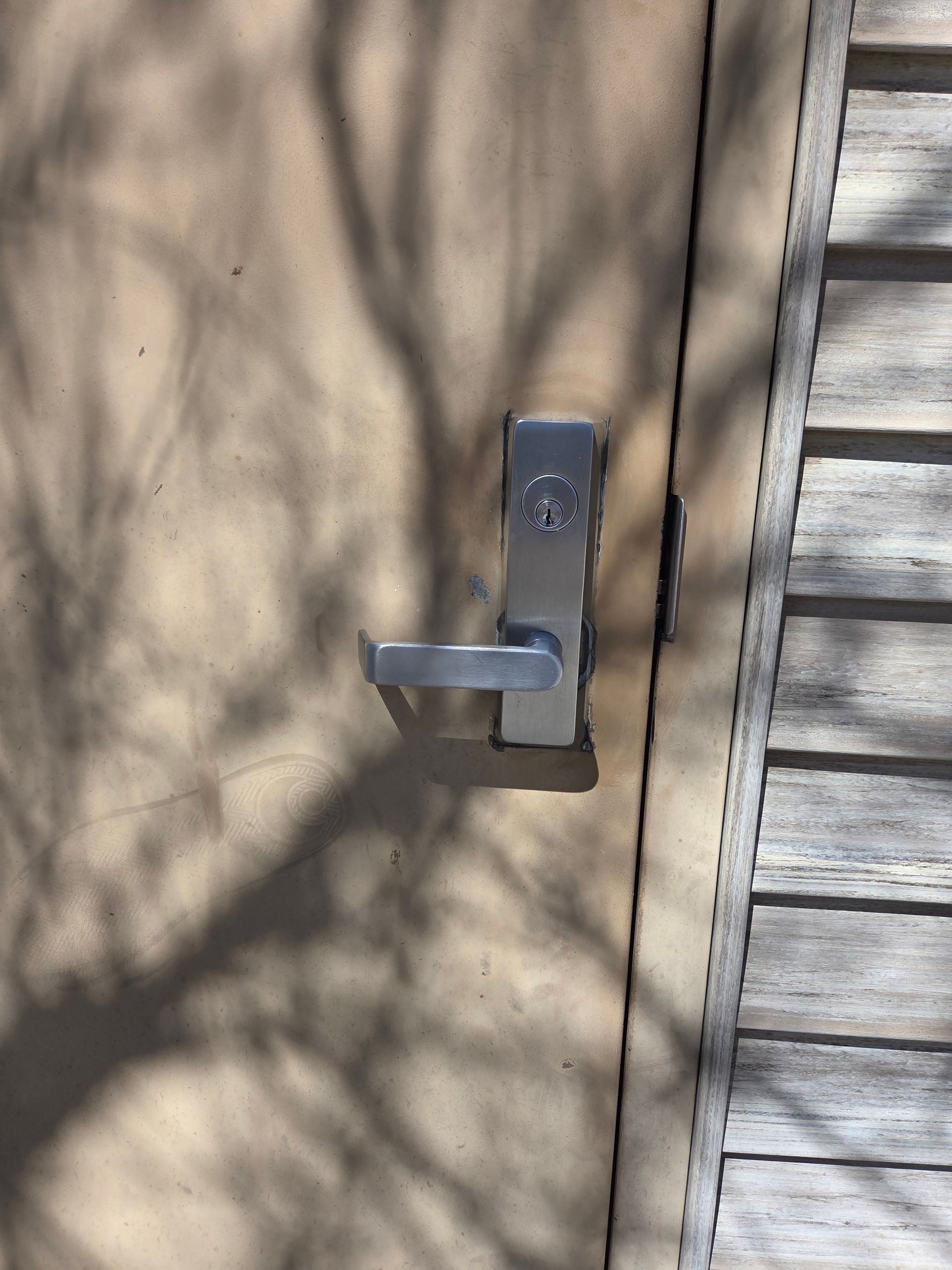 Silver door handle on beige exterior door beside white siding, with tree shadows cast across it
