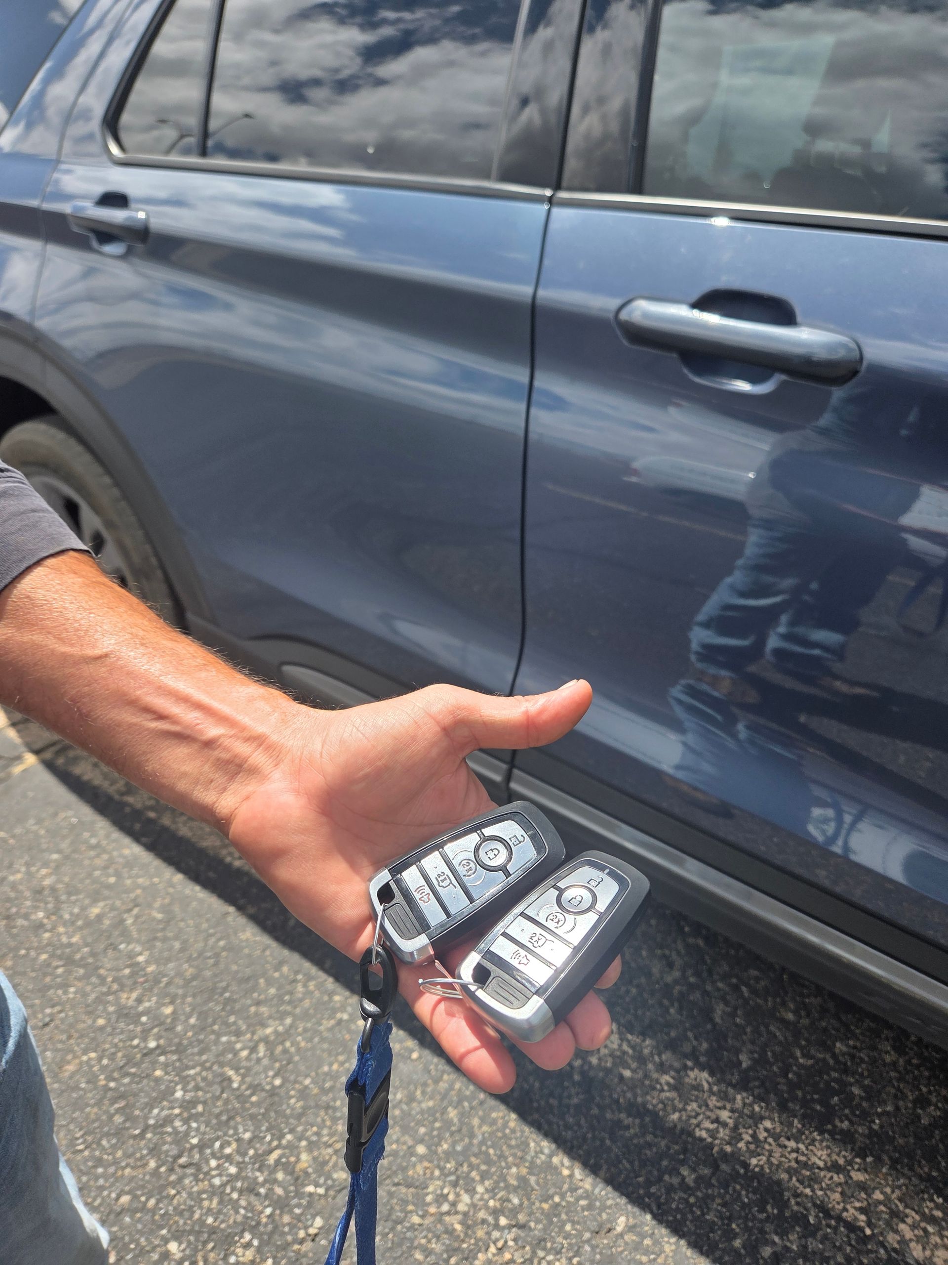 Hand holding a car key fob beside a blue SUV door and handle