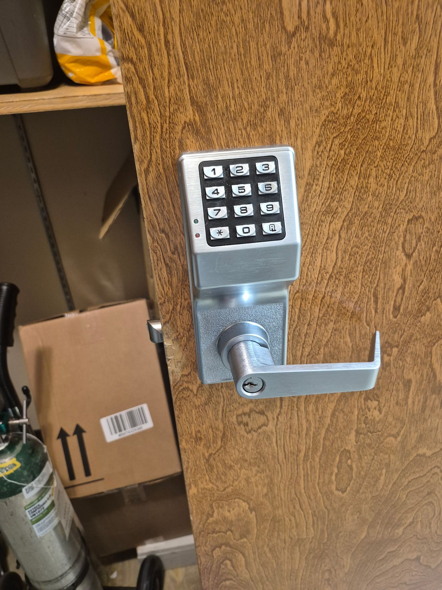 Keypad door lock on a brown wooden door, with storage shelves visible beside it.