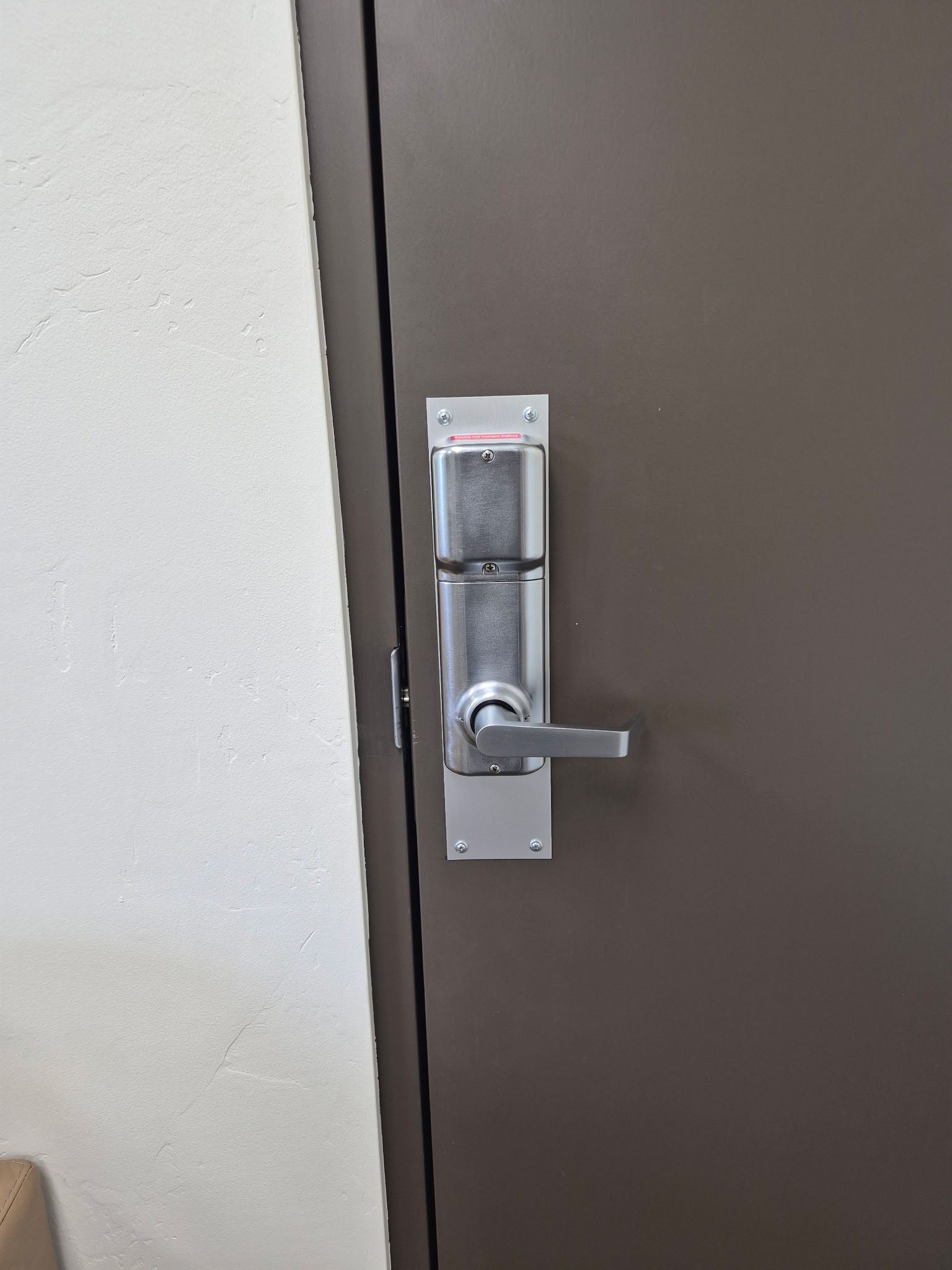 Close-up of a silver door lever and lock on a beige doorframe.