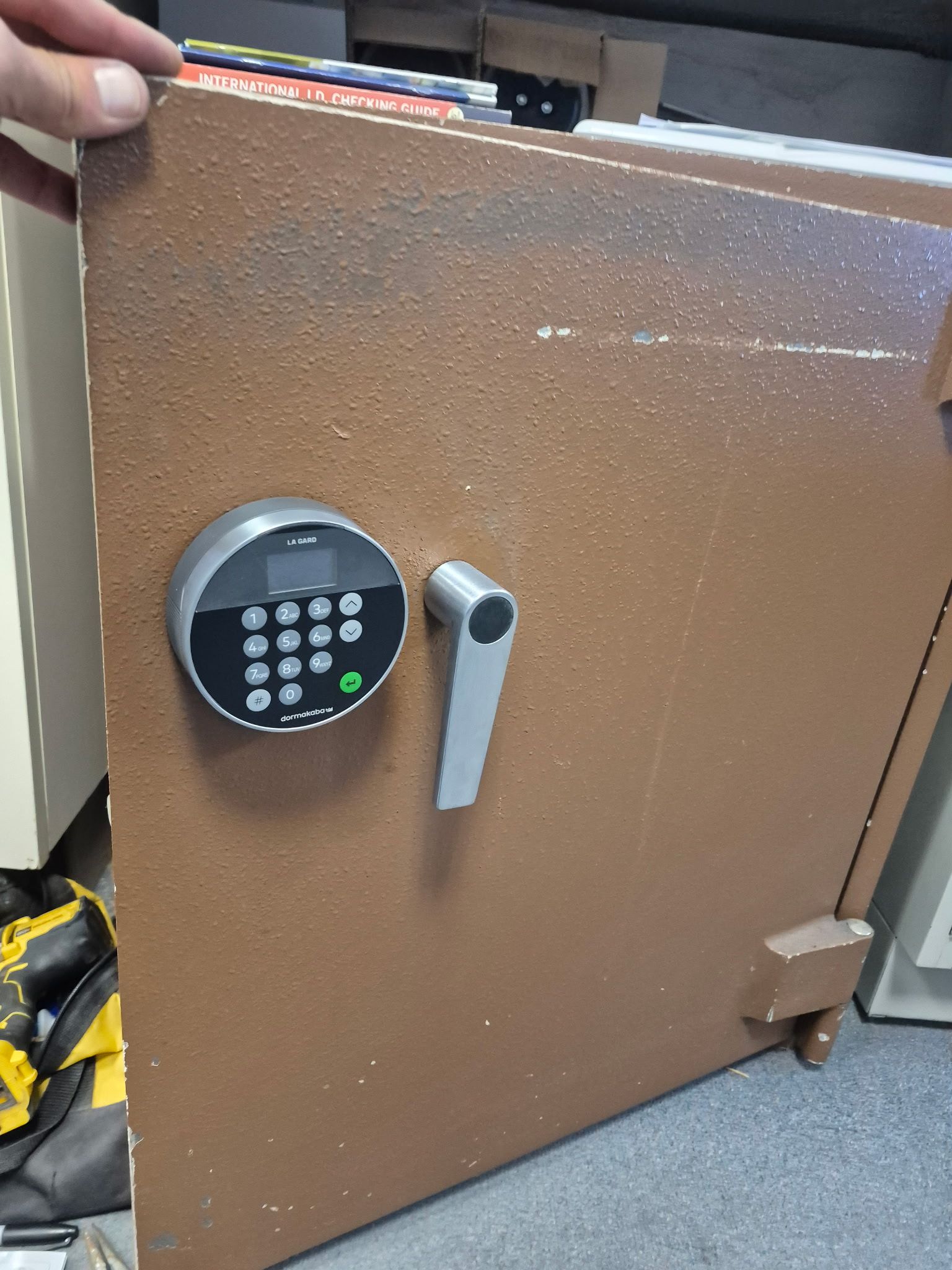 Brown metal safe with electronic keypad and handle, partially open in a carpeted room.