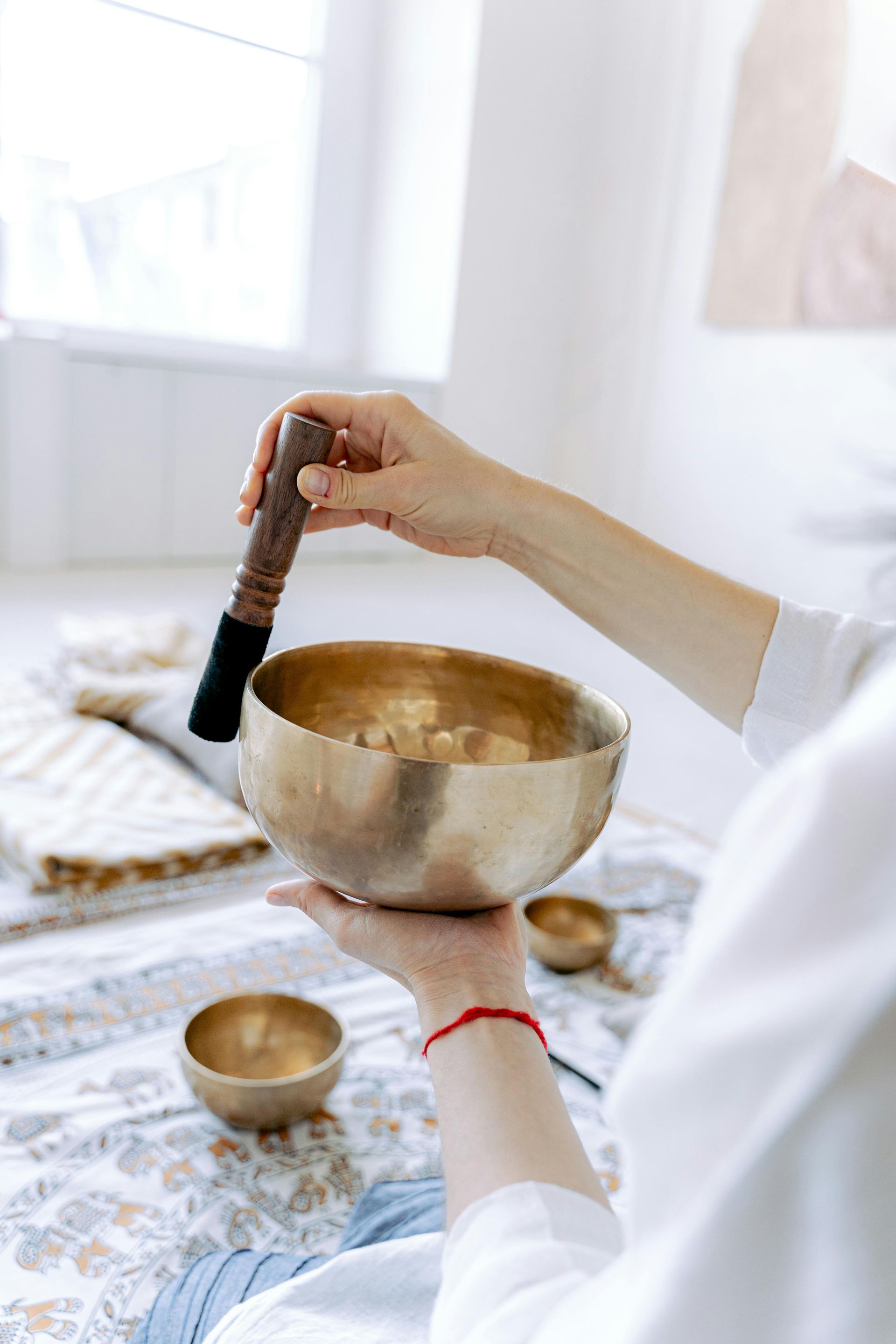 Person holding a golden singing bowl, striking it with a mallet. Interior, light setting.