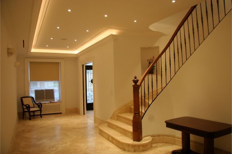 Spacious beige foyer with curved staircase, recessed ceiling lights, and a chair near a window