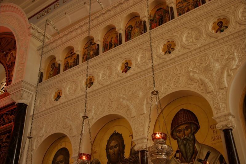 Ornate church interior with carved white arches, icons, and a red light near the altar