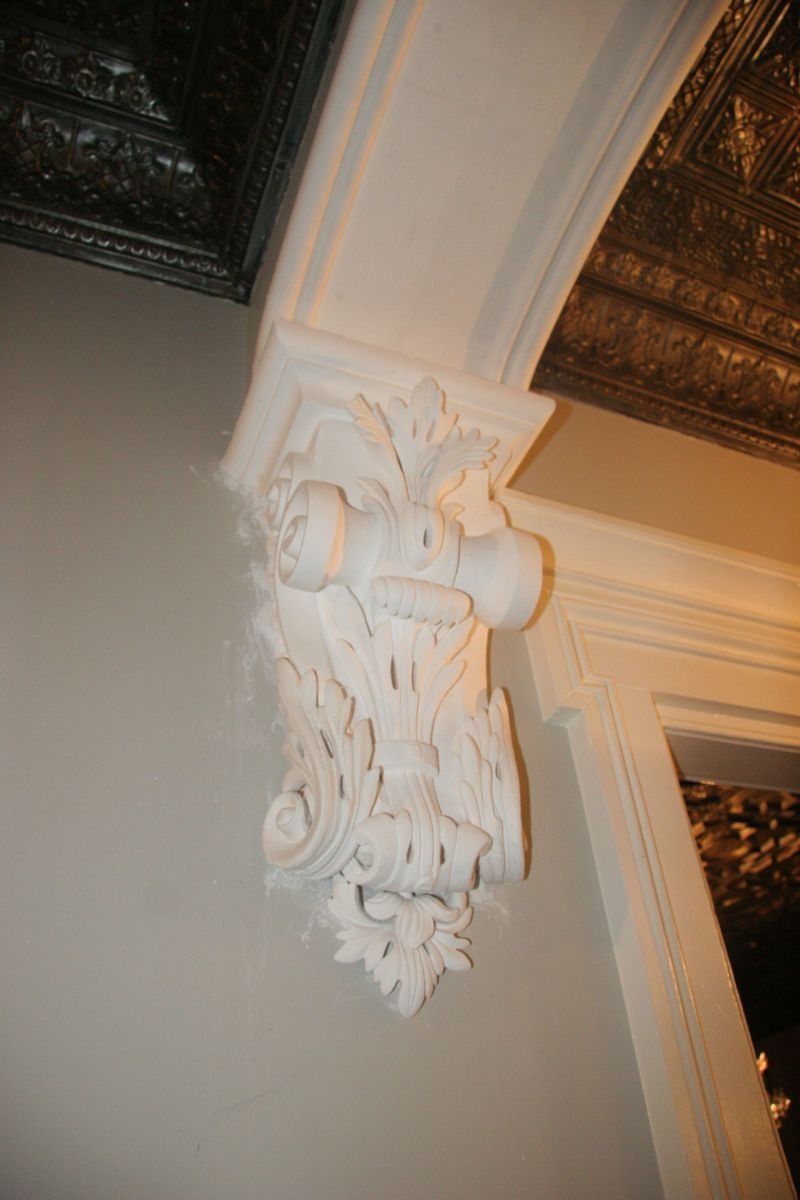 Ornate white carved architectural corbel supporting a ceiling beam indoors