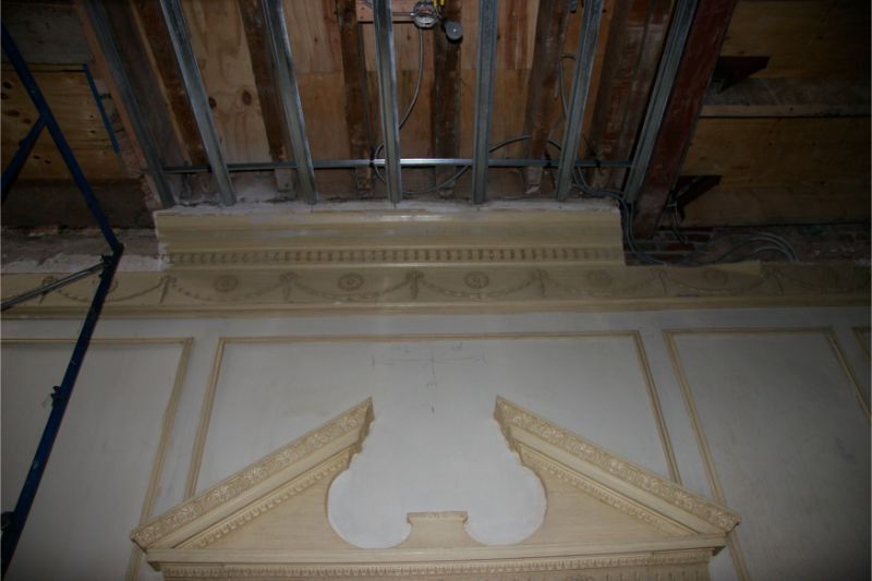 Ornate white wall molding and pediment beneath exposed wooden beams on a ceiling.