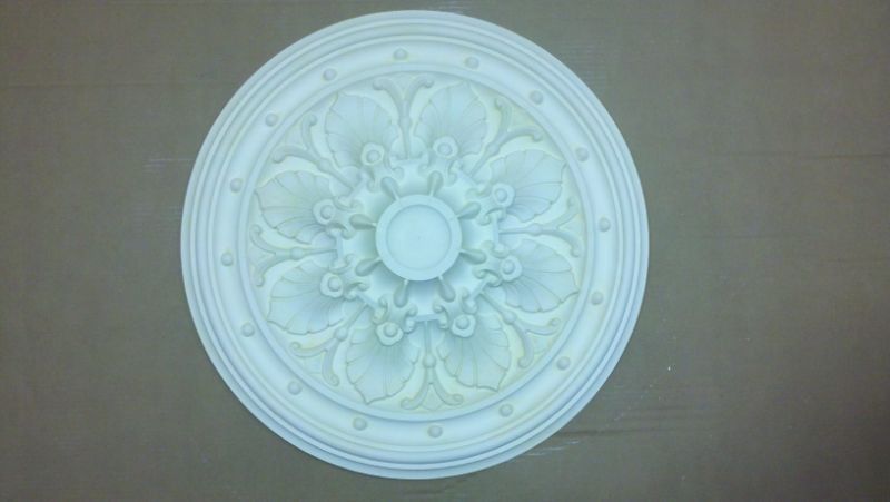 White decorative ceiling medallion with floral relief on a beige wall background