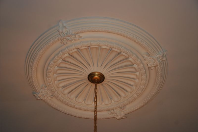 Ornate white ceiling medallion with a brass light fixture and pull chain