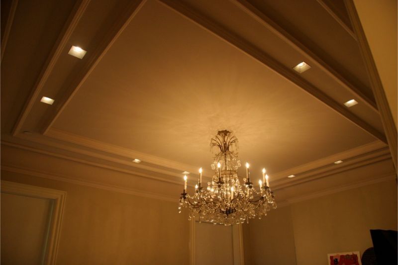 Chandelier hanging from a vaulted ceiling with warm recessed lighting in a beige room