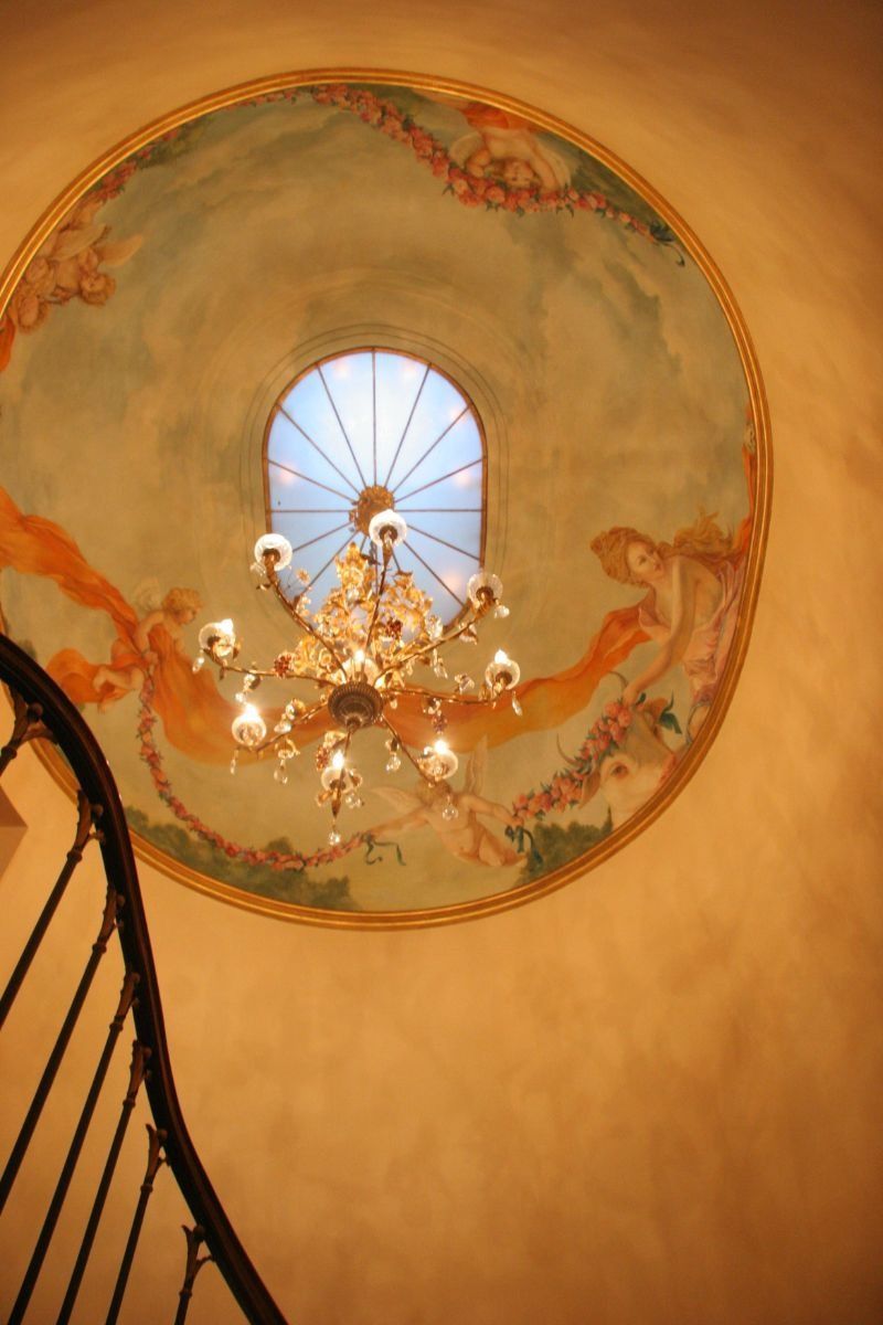 Chandelier beneath a circular painted ceiling mural with warm orange and blue tones