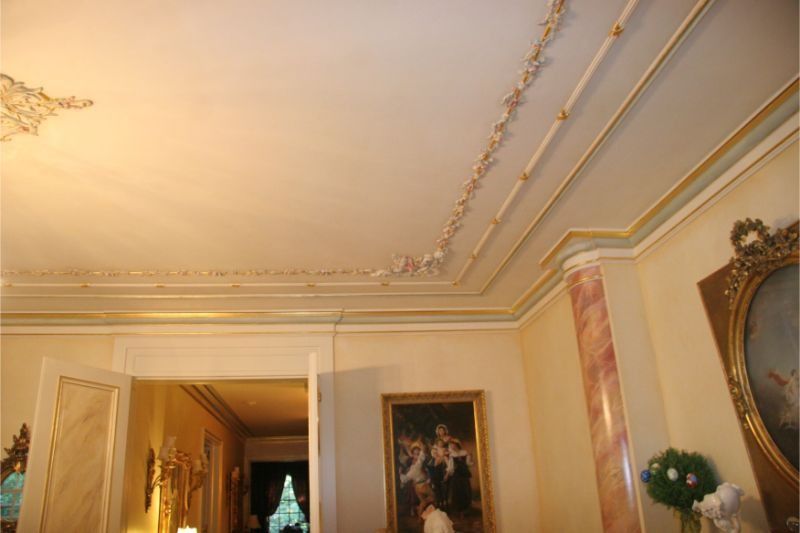 Elegant room interior with ornate ceiling moldings, chandelier light, and framed wall art