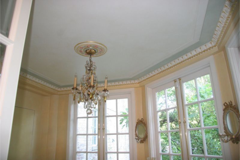 Elegant room with ornate chandelier, cream walls, and tall windows overlooking greenery