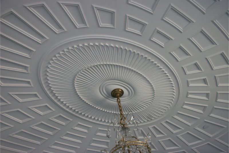Decorative white ceiling with ornate circular molding and a chandelier hanging at center