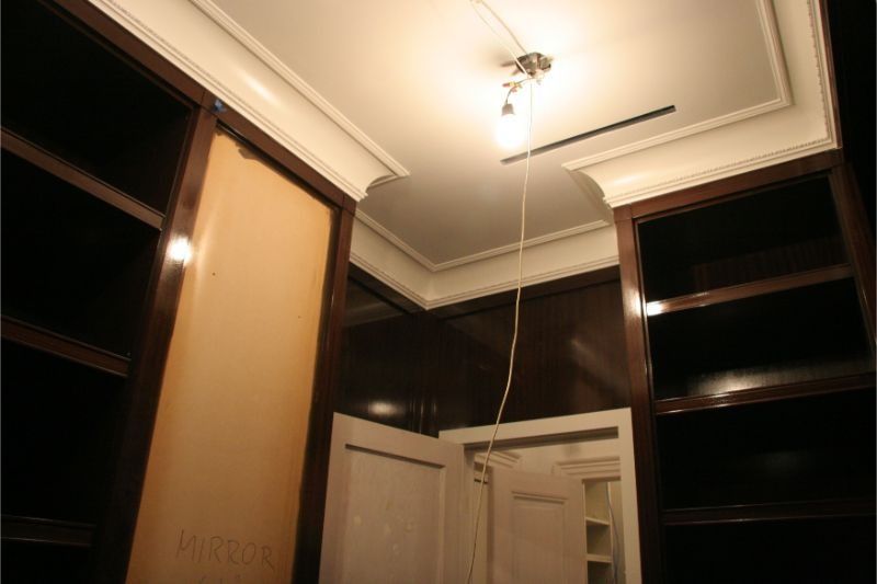 Walk-in closet with dark wood shelves, beige walls, and a ceiling light fixture