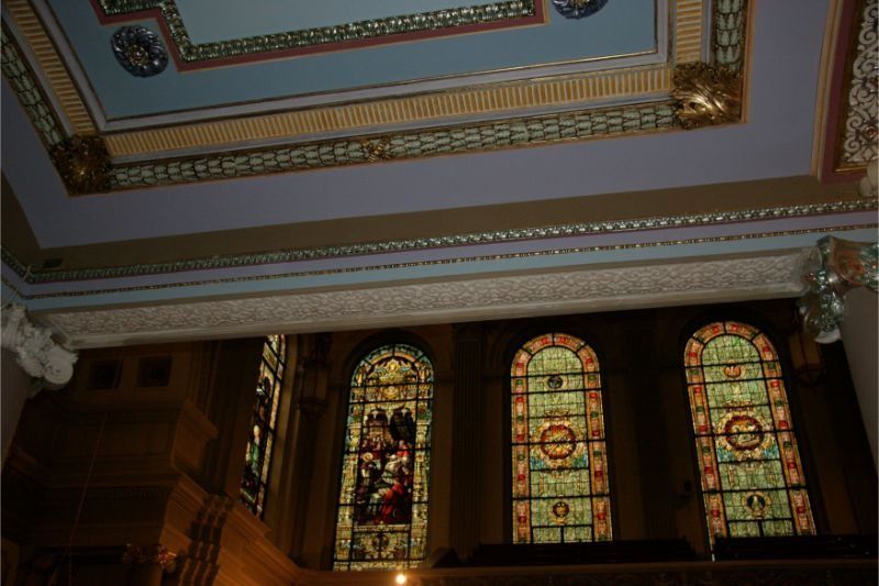 Interior ceiling with ornate stained-glass windows and decorative molding in a dimly lit room