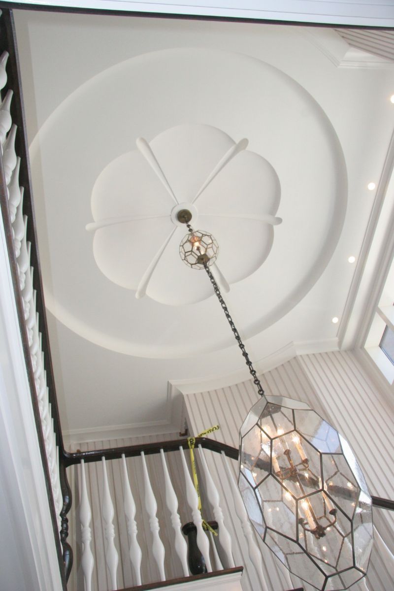 Ceiling medallion and hanging geometric pendant light in a white interior stairwell.