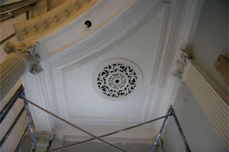 Ceiling with ornate plaster molding and a circular decorative medallion, viewed from below.