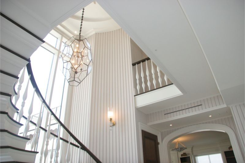 White staircase and hallway with curved railings, striped walls, and a hanging geometric light fixture