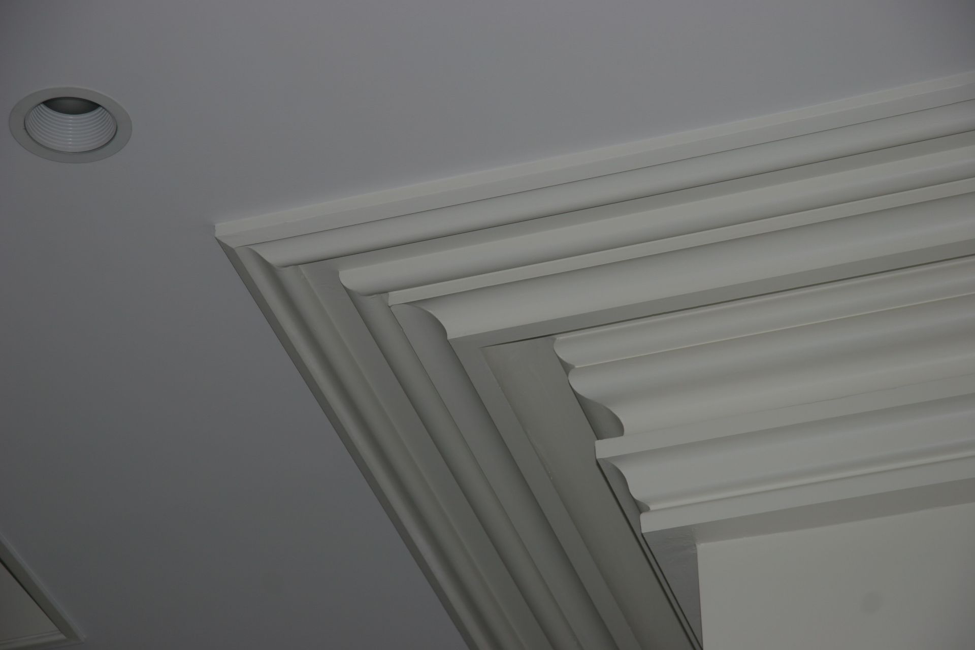 White ceiling corner with layered decorative crown molding and a recessed light fixture