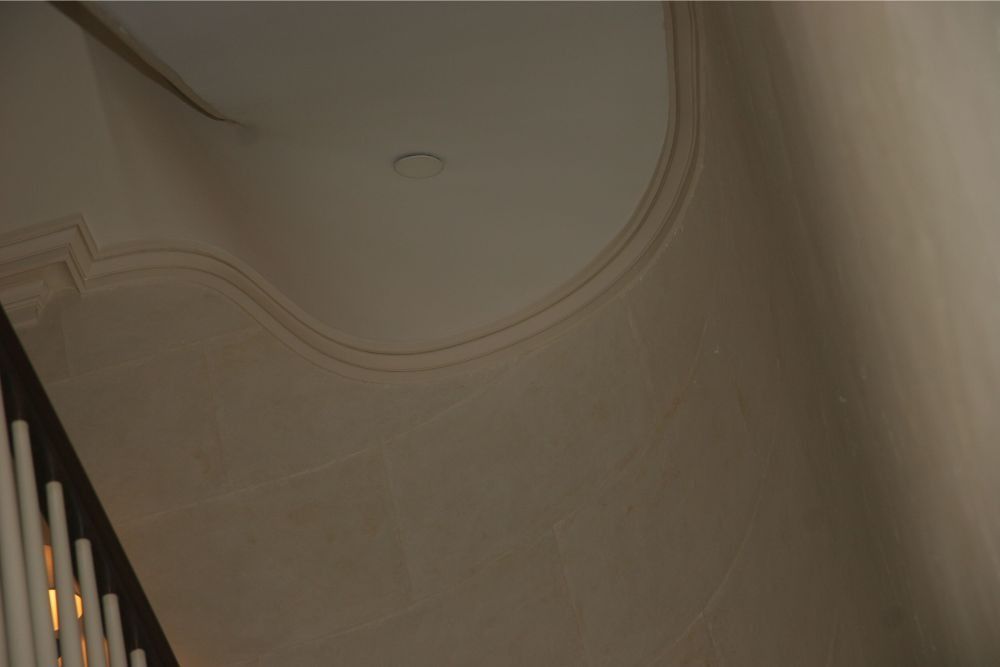 Curved beige ceiling with decorative molding and a small recessed light above a staircase railing