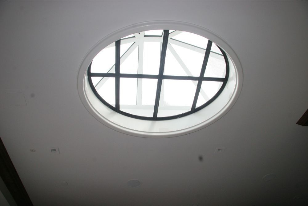 Oval skylight in a white ceiling with metal framing, letting daylight into a room