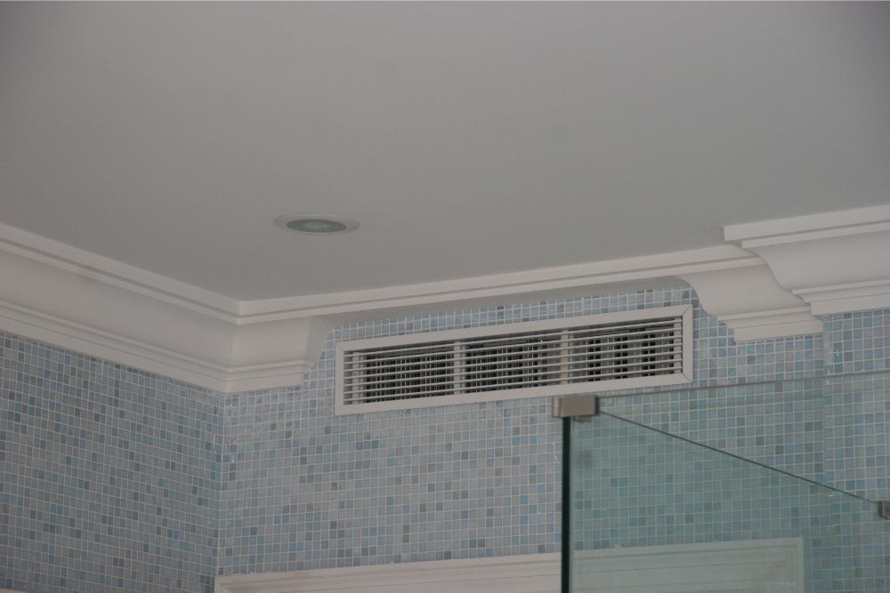 Ceiling vent above blue tiled bathroom wall with white crown molding