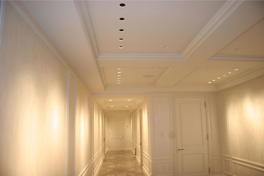 Elegant white hallway with ornate ceiling, recessed lights, and doors along the right wall.