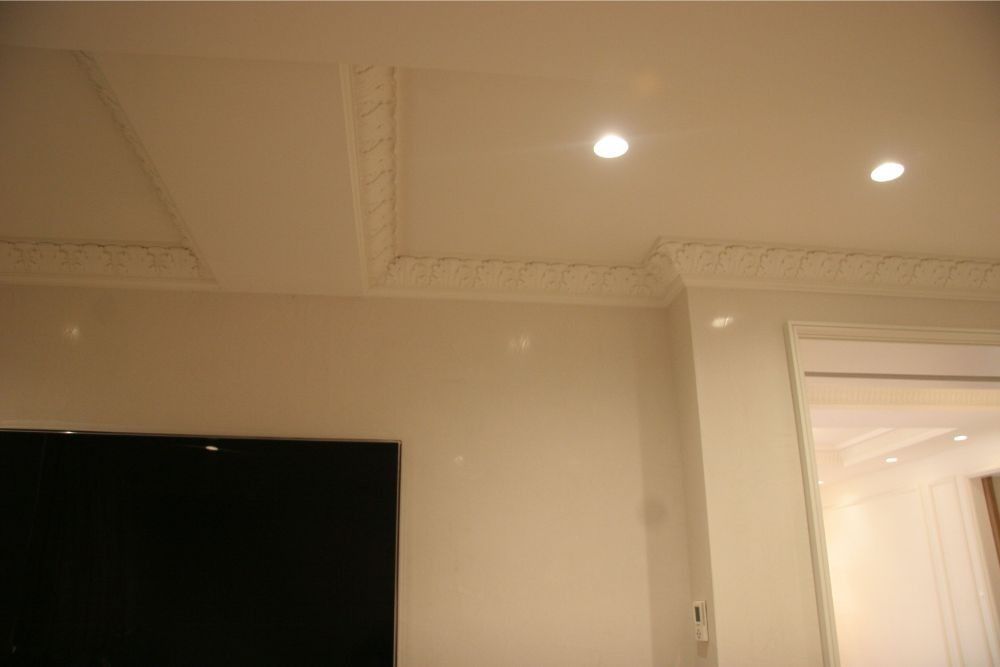 Ceiling with ornate molding, recessed lights, and a doorway beside a wall-mounted TV screen