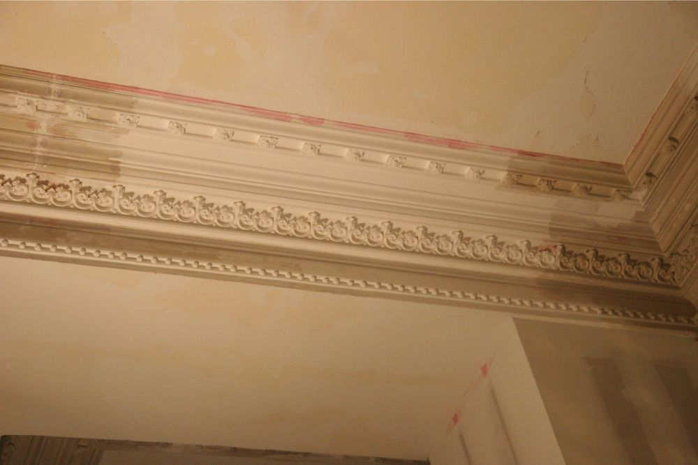Decorative white crown molding along a beige ceiling with ornate plaster details