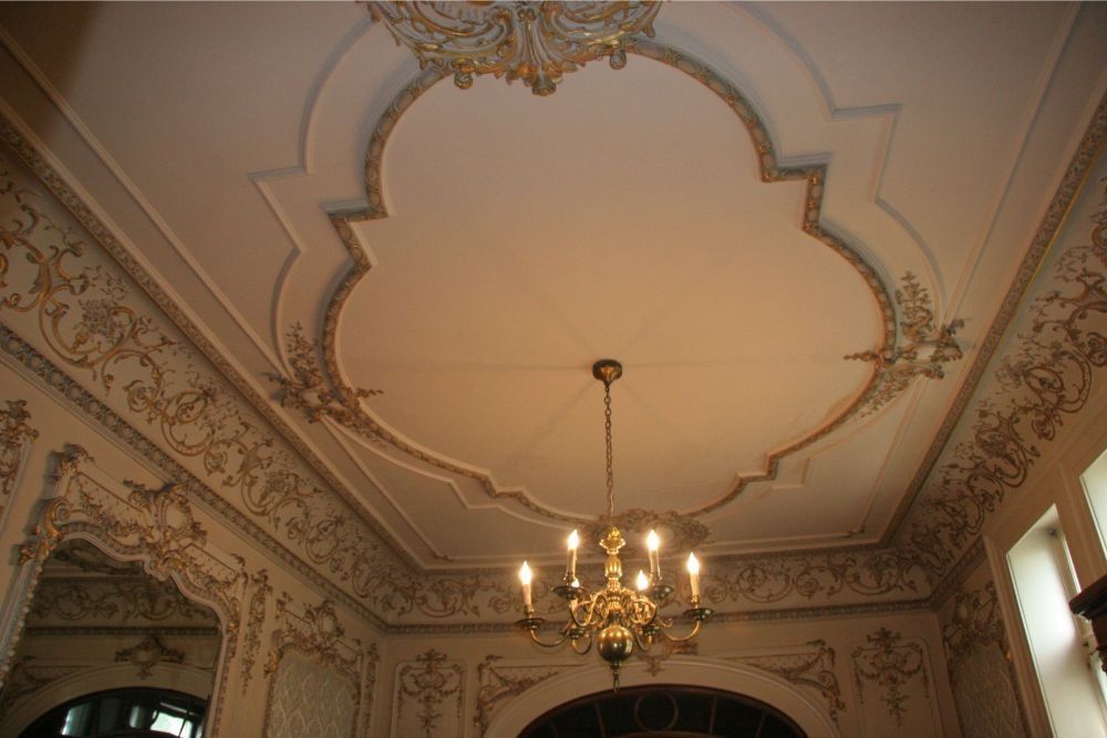 Ornate ceiling with gold trim and a hanging chandelier in a decorated room