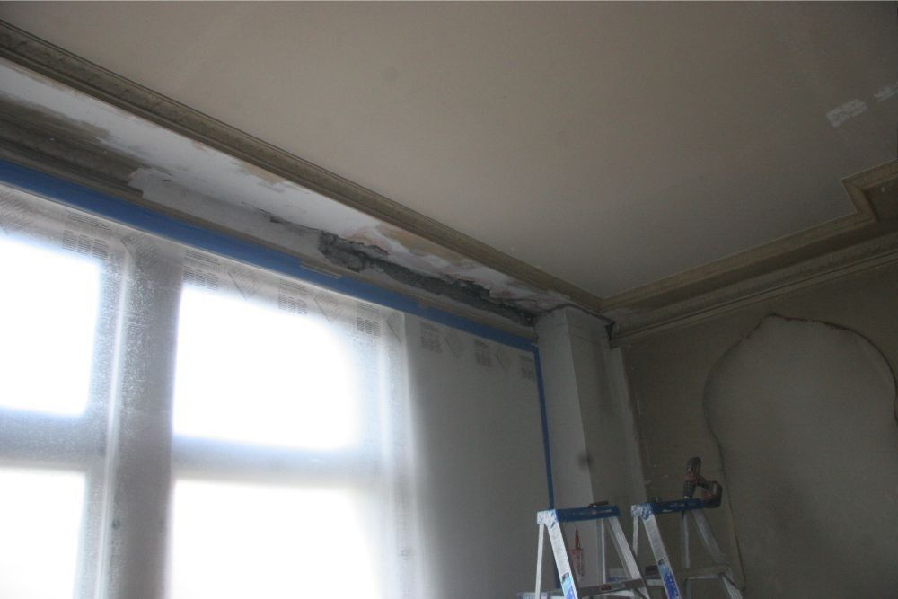 Renovation room with masked window, ceiling trim, and a ladder beneath a bare wall curve