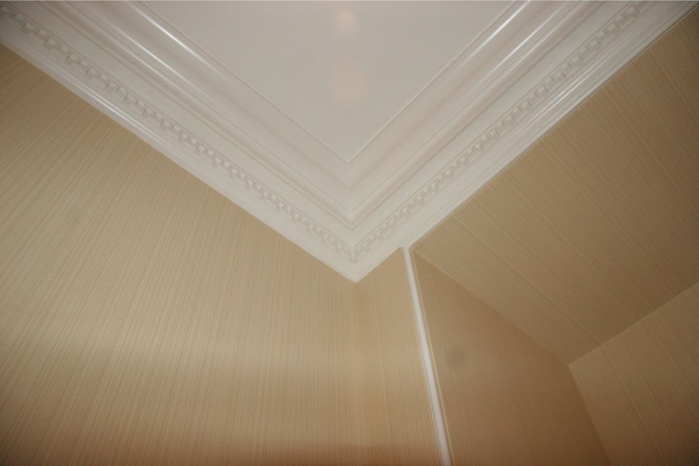 Corner of a room with beige striped wallpaper and ornate white crown molding on the ceiling