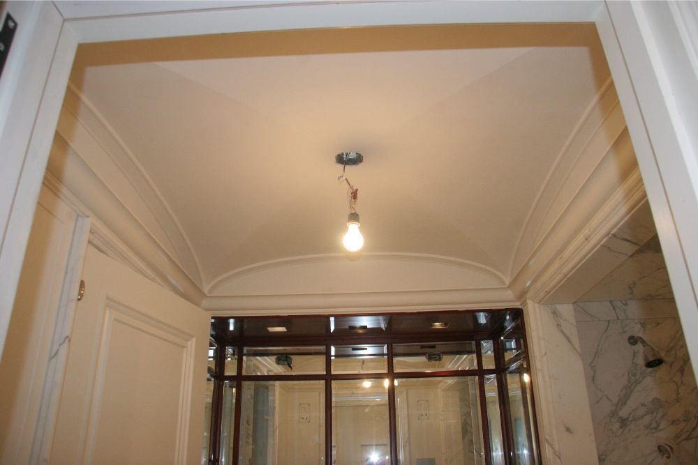 Hallway ceiling with hanging light bulb, white trim, and doorway opening into another room