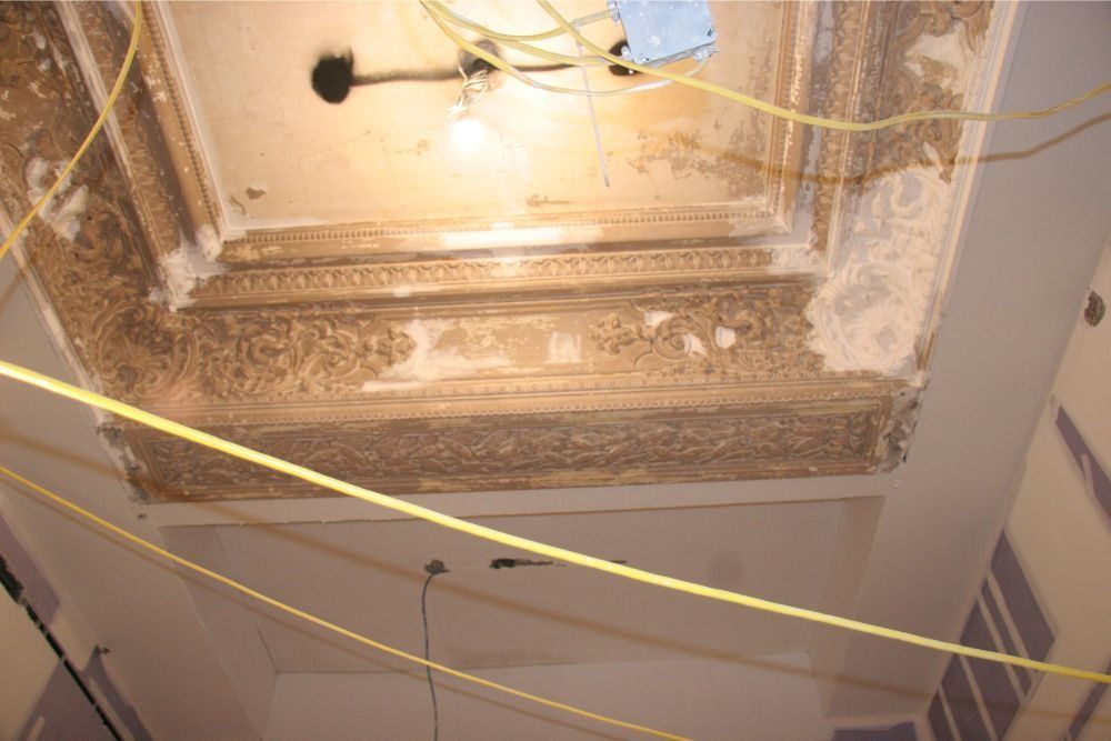 Damaged ceiling with exposed wires, peeling plaster, and a hanging light fixture above a room