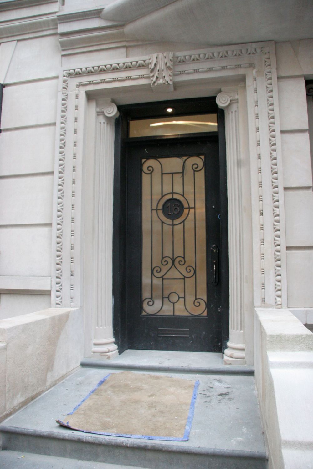 Stone building entrance with ornate black wrought-iron door and doormat on a small step