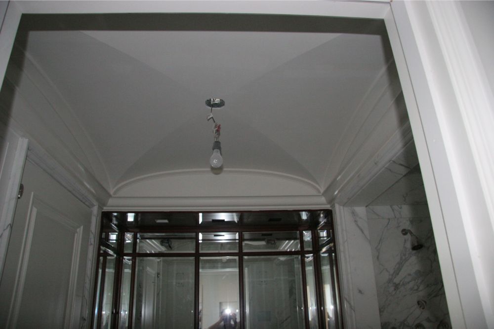 Interior doorway with white trim, a hanging light bulb, and a glass enclosure in the background