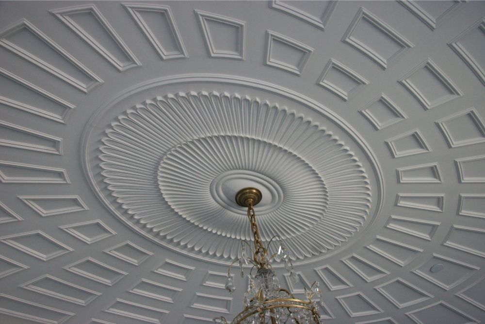 Ornate white ceiling with geometric plaster patterns and a chandelier hanging from the center