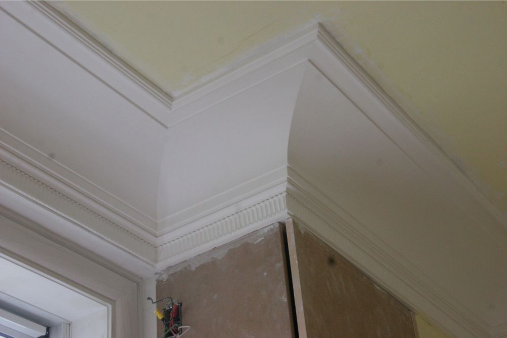 White crown molding and ceiling corner above a doorway, with unfinished wall paneling below