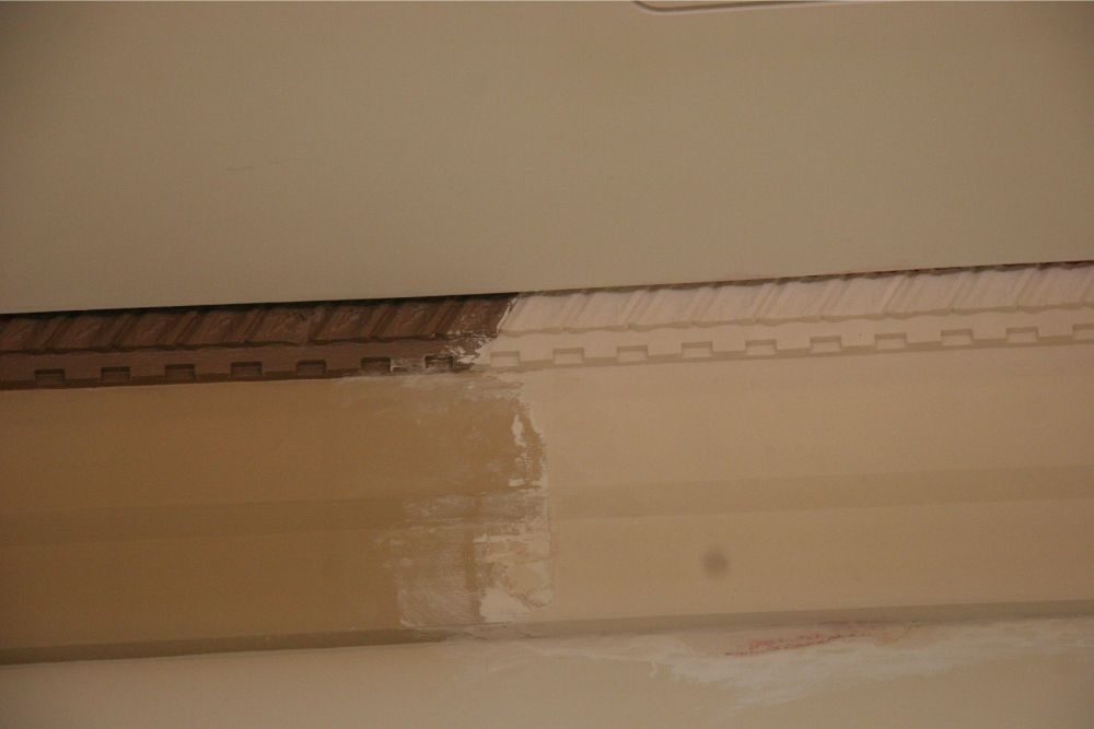 Close-up of a damaged wall or ceiling with peeling paint and exposed material at the top edge
